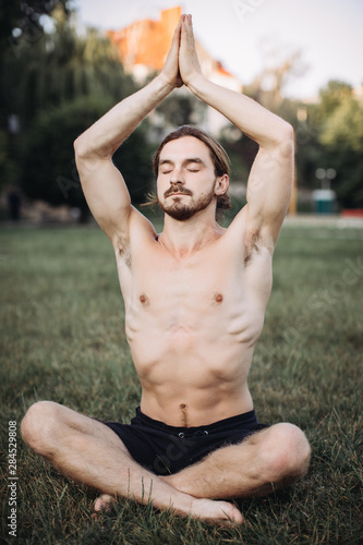 Yoga at park. Bearded man in lotus pose sitting on green grass. Concept of calm and meditation. photo