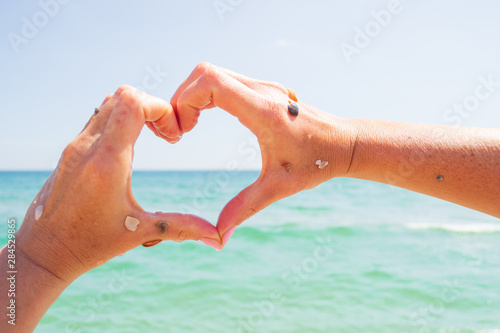 Wet female hands show a heart on a background of blue sea