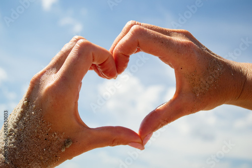 Wet female hands show a heart on a background of blue sky