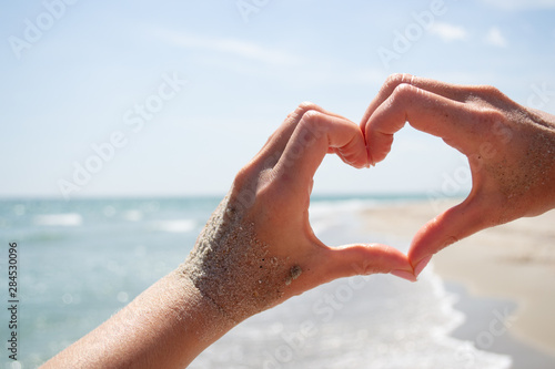 Wet female hands with the sand show a heart on a background of blue sea