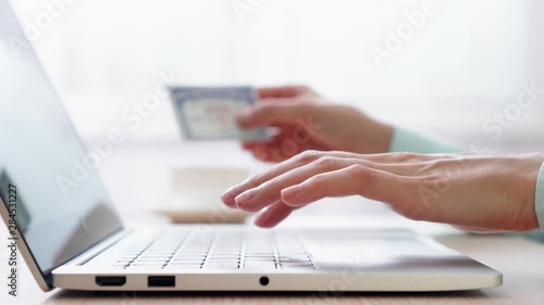 Woman freelancer typing on laptop at home-office. Blurred female hand holding social security number on background. Businesswoman filling out tax return form online at work. Dolly shot photo