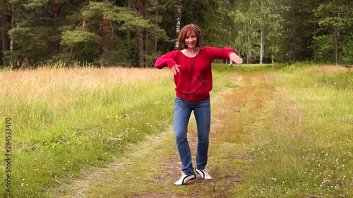 A young beautiful girl in a red blouse and blue jeans listens to music with headphones and dances in a city Park on a summer day