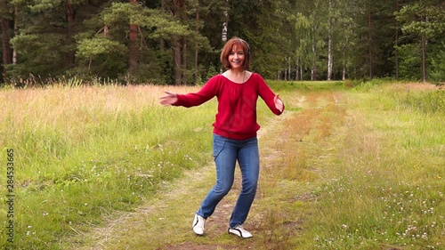 A young beautiful girl in a red blouse and blue jeans listens to music with headphones and dances in a city Park on a summer day