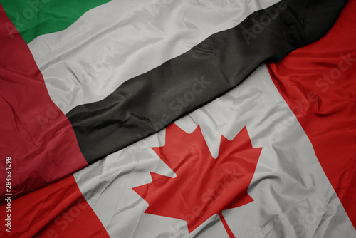 waving colorful flag of canada and national flag of united arab emirates.