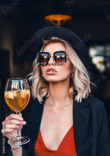 Beautiful girl in drinks Aperol Spritz wine from a glass in a restaurant, a cafe, has a good weekend, a stylish fashionable woman, a brunette young, emotional, outdoor close up hipster portrait
