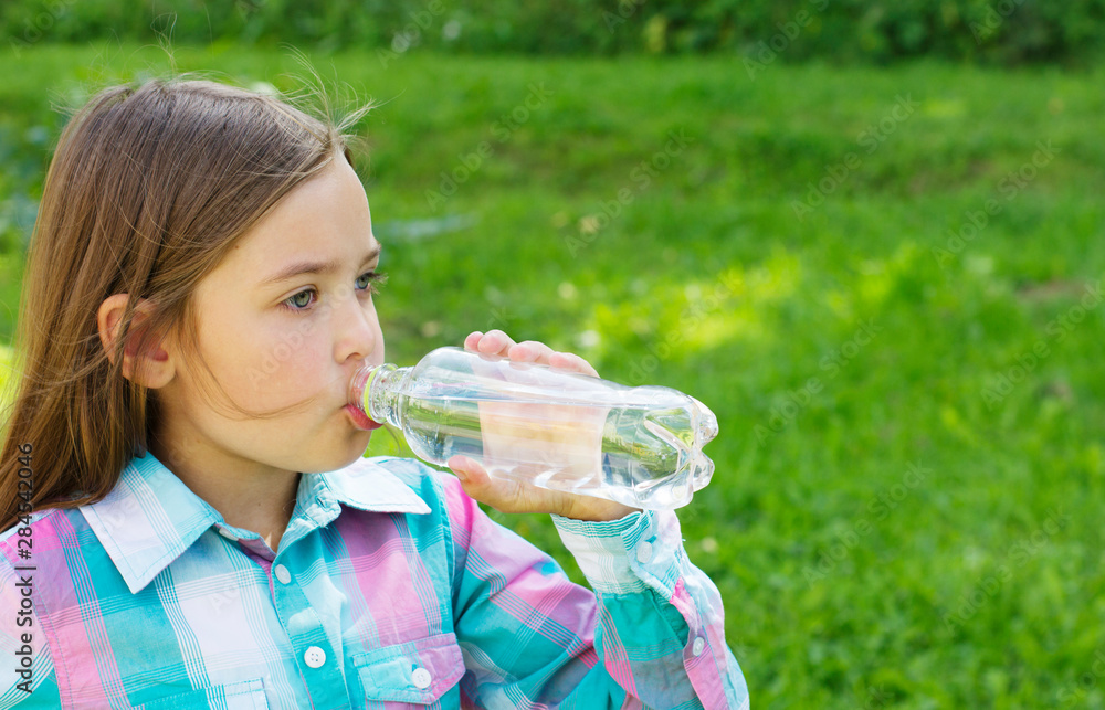  Cute little girl drinks water from a bottle.