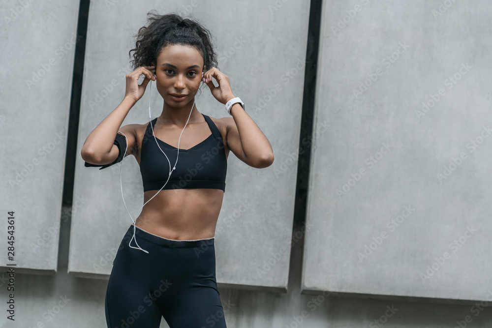 Fototapeta premium Fitness woman taking a break from outdoor training session with earphones and look in camera