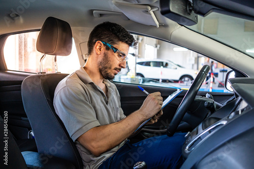Technician with safety glasses sitting in a car seat checking a list during a vehicle inspection photo