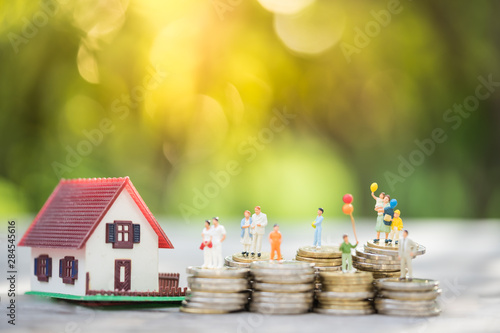 Miniature people: family standing on coins stacks with  house model on the top stack.  concepts. Concept for property ladder, mortgage,real estate investment, money, love and Valentine's day.