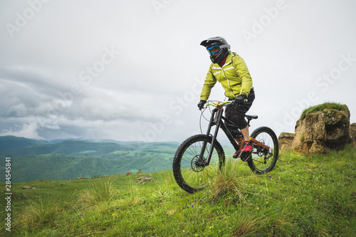 Front view of a man on a mountain bike standing on a rocky terrain and looking down against a gray sky. The concept of a mountain bike and mtb downhill