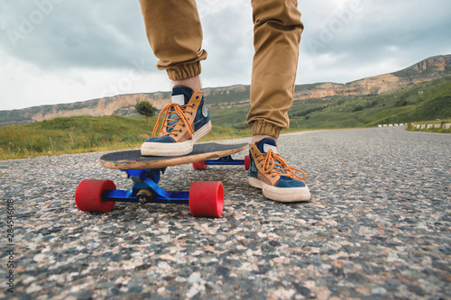 Close-up of male legs in rag sneakers on a longboard on the background of asphalt at sunset. Big skateboard with man legs. Youth leisure concept