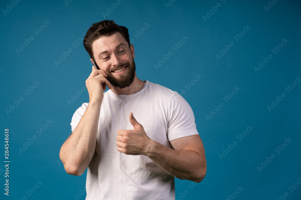 casual man showing thumb up sign while talking on the telephone and smiling for the camera. isolated on blue background casual man showing thumb up sign while talking on the telephone and smiling for the camera. isolated on blue background
