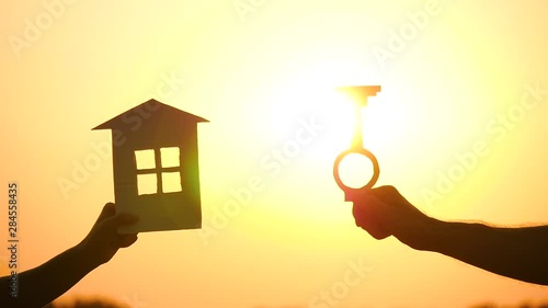 Silhouette of hands holding model house and key on sunset background. The concept of construction and real estate transactions. photo