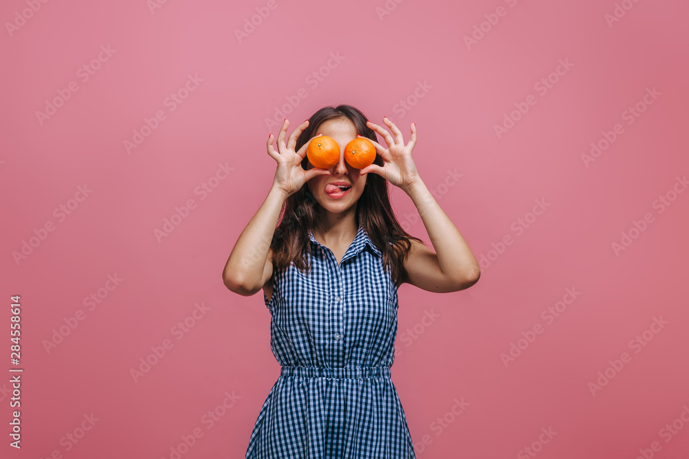 Girl closed her eyes with oranges and shows tongue on pink background Girl closed her eyes with oranges and shows tongue on pink background