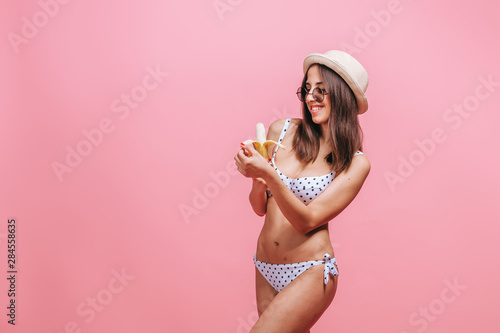 Girl eating a banana on a pink background.