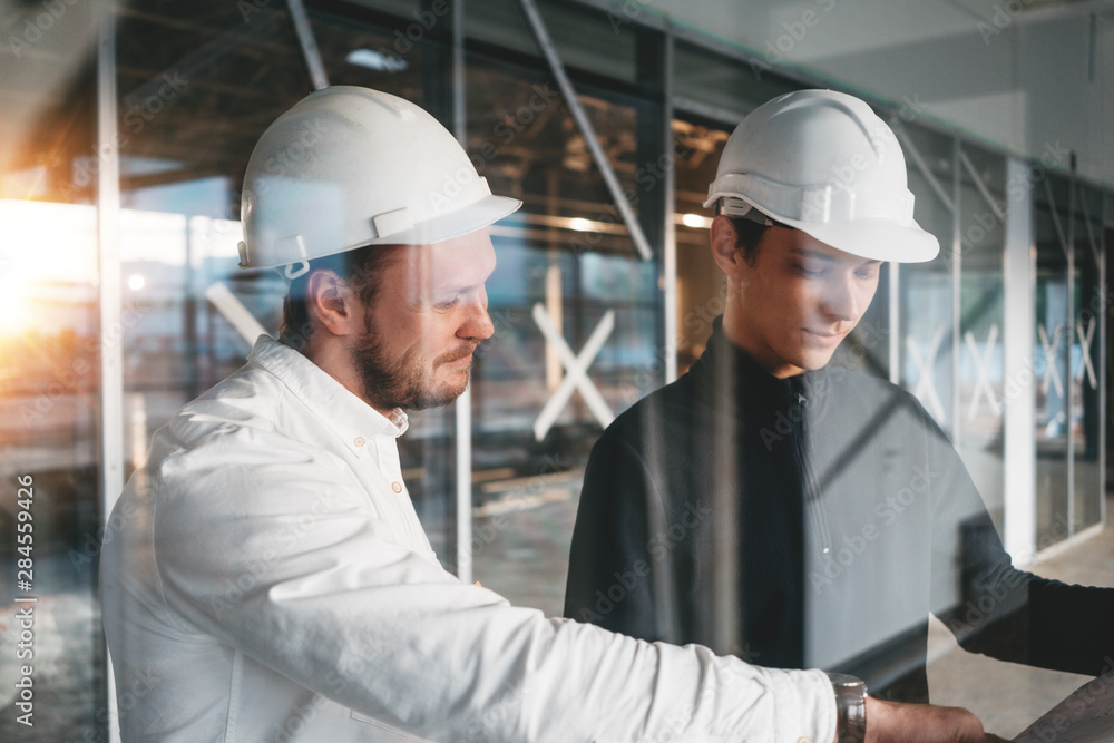 Building engineer and worker hold blueprint in hand while discussong construction site. Industrial engineers have meeting on build Building engineer and worker hold blueprint in hand while discussong construction site. Industrial engineers have meeting on build