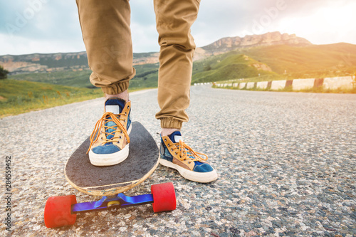 Close-up of male legs in rag sneakers on a longboard on the background of asphalt at sunset. Big skateboard with man legs. Youth leisure concept