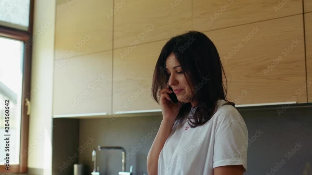 Portrait woman in talking on cellphone and drinking coffee in kitchen in the morning cellphone communication conversation indoors kitchen modern happy holding lifestyle looking speaking slow motion Portrait woman in talking on cellphone and drinking coffee in kitchen in the morning cellphone communication conversation indoors kitchen modern happy holding lifestyle looking speaking slow motion
