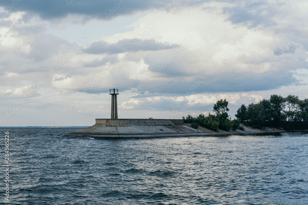 Fototapeta premium Lighthouse on edge of concrete breakwater on wide river