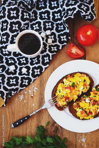 hearty and healthy breakfast, scramble eggs with tomatoes and herbs on toast with black tea on a wooden background