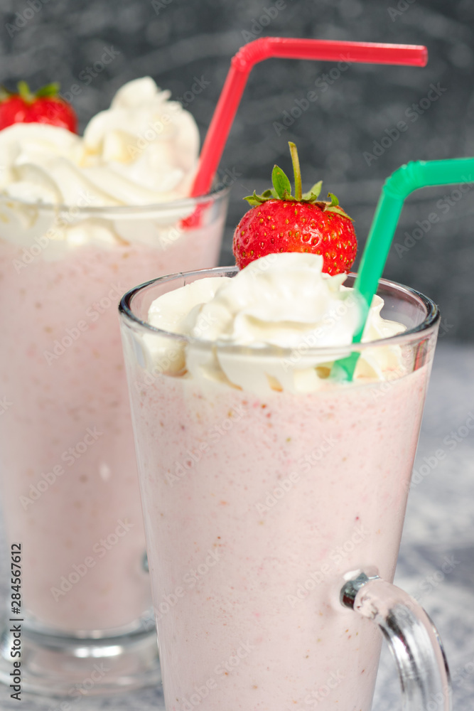 Two glasses with strawberry milkshake with pieces of berries on the edge of the glass on gray background. Two glasses with strawberry milkshake with pieces of berries on the edge of the glass on gray background.