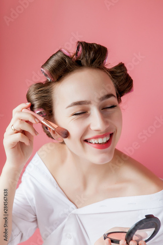 Eyeliner eye makeup beauty care woman. Girl putting eye pencil color on eyes looking in a pocket mirror smiling happy on pink background.