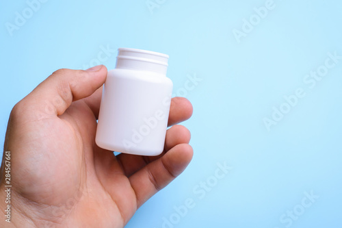 Man`s hand holds white plastic bottle for pills against light blue background. Concept of medicine, pills, health care, treatment. Copy space for inscription