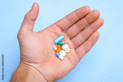 Concept of taking pills. Man`s hand holding different pills capsules against blue background