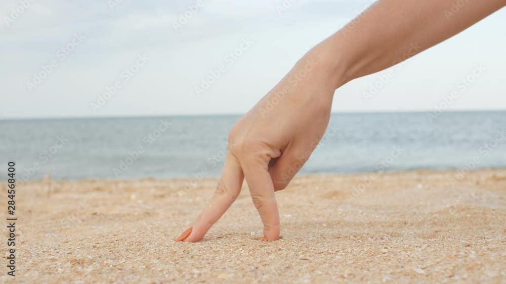 female fingers walk on the sand against the background of the sea imitating a man’s gait, hand make step, playing on the beach, fun concept female fingers walk on the sand against the background of the sea imitating a man’s gait, hand make step, playing on the beach, fun concept