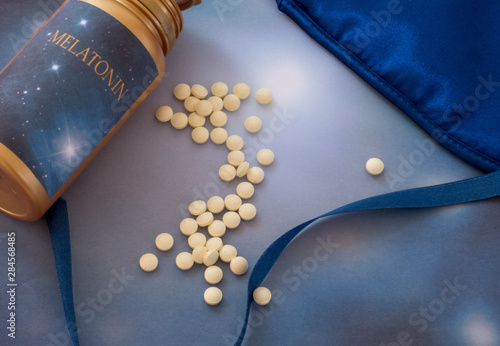 Melatonin supplements and sleep mask on the blue background.