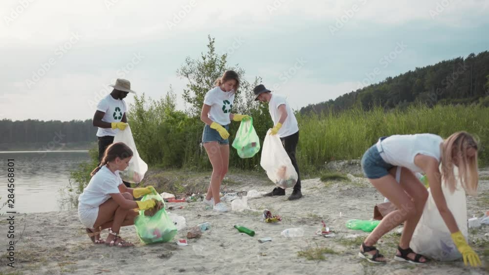 Save the planet. Team of vigorous recycling volunteers ccollecting plastic rubbish into bags on lake beach cleaning up nature landscape. Save the planet. Team of vigorous recycling volunteers ccollecting plastic rubbish into bags on lake beach cleaning up nature landscape.