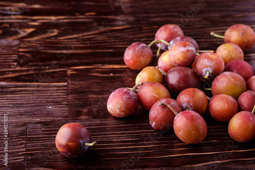 Scattered ripe sweet plum fruits on dark moody wood table background, soft light, copy space