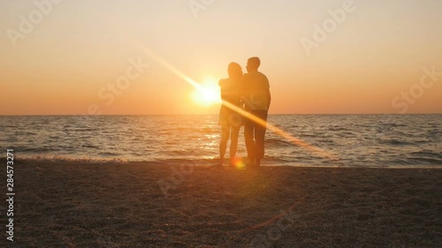 silhouette of a romantic young couple standing on the seashore, man hugging girl at sunrise on the beach, courtship on summer vacation and honeymoon