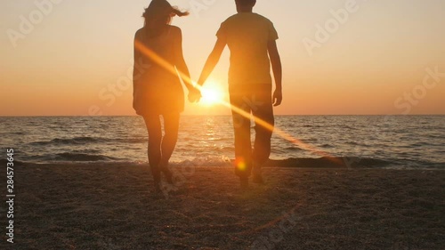 silhouette of a romantic young couple standing on the seashore, man comes up and takes the girl's hand and together enjoying sunrise on the beach, summer vacation and love photo