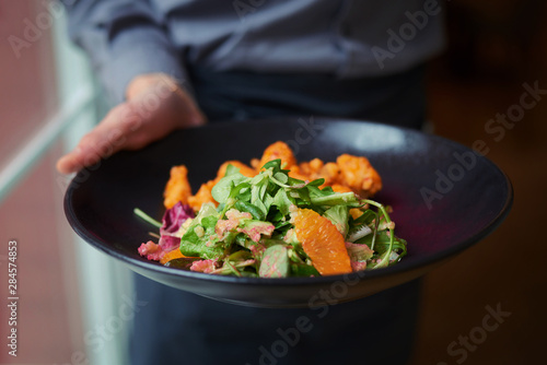 Waiter holding plate with salad in one shape