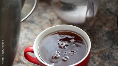 Pouring water from a kettle into a mug. Hot water in a white tea mug with tea bag on a black background. Top view with steam rising from a cup. red mug
