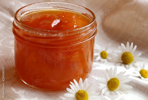  Homemade  organic apricot jam in glass jar  on the background of a white tablecloth with daisy flowers. 