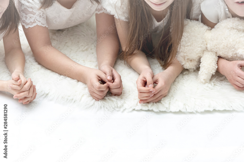 Bright view of children based on elbows on white background.Adorable little girls in white dresses lying on the floor. Happy kids. Bright view of children based on elbows on white background.Adorable little girls in white dresses lying on the floor. Happy kids.