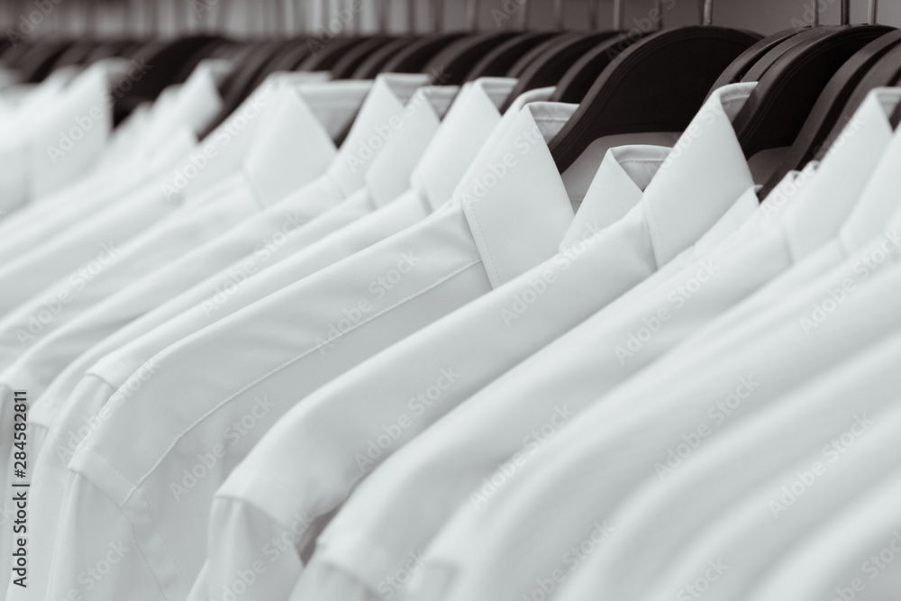 Fototapeta premium Row of white shirts hang on black hangers on a rack in a shop. A close-up.