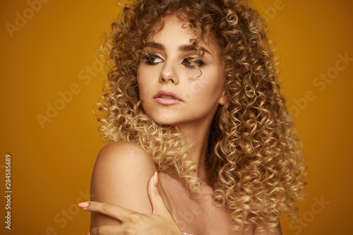 Beauty portrait of young girl with afro hairstyle. Girl posing on yellow background. Studio shot