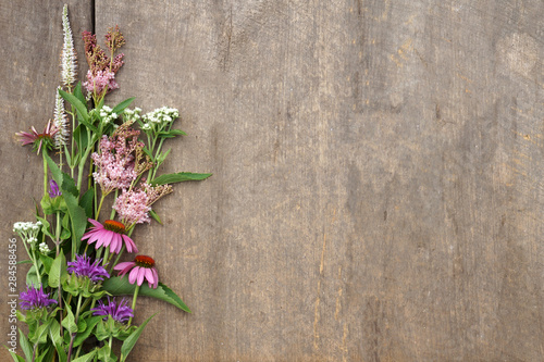 Horizontal image of a bunch of fresh cut perennial flowers in shades of pink and white on a weathered wood background, with copy space