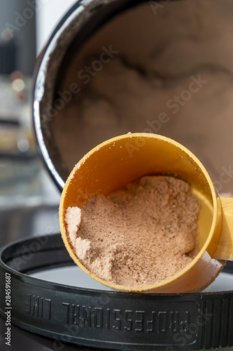 Plastic measuring spoon and heap of brown chocolate protein powder. Sport nutrition concept