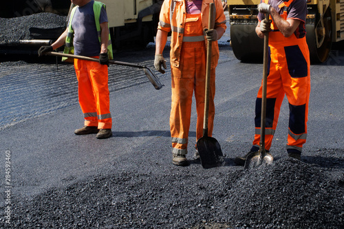Workers in orange uniform are laying asphalt on a city street. Road machinery