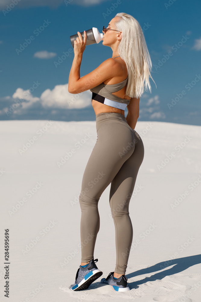 Fitness woman drinking water, outdoor. Athletic girl quenches thirst.  Beautiful female in leggings with sexy butt foto de Stock | Adobe Stock