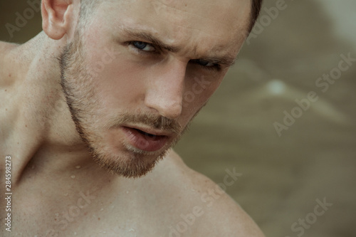Strong face male model on the nature background with sand and water on the beach on the sunset