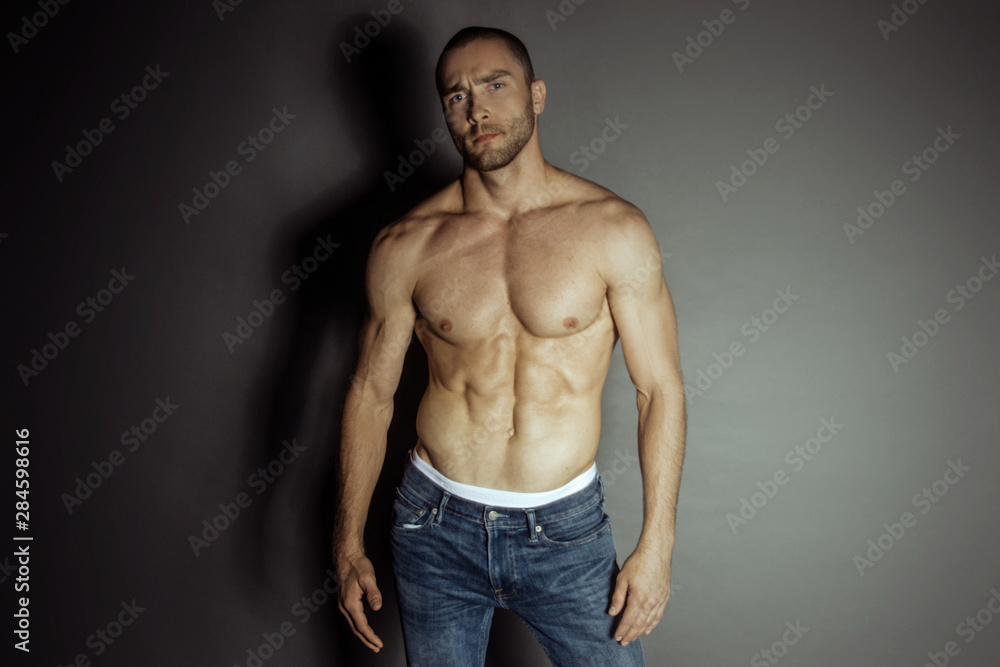 Muscle strong beautiful stripped male model with white underwear in denim blue jeans on black isolated font 