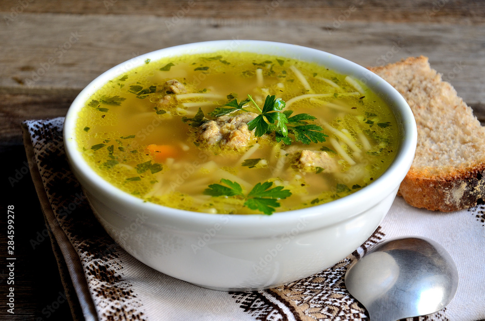 Homemade soup with meatballs and noodles, folk napkin on a wooden table.