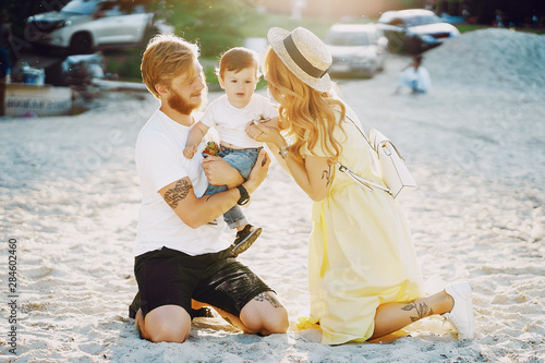 Beautiful red-haired woman with her husband and a wonderful son sitting on a summer beach on the sand