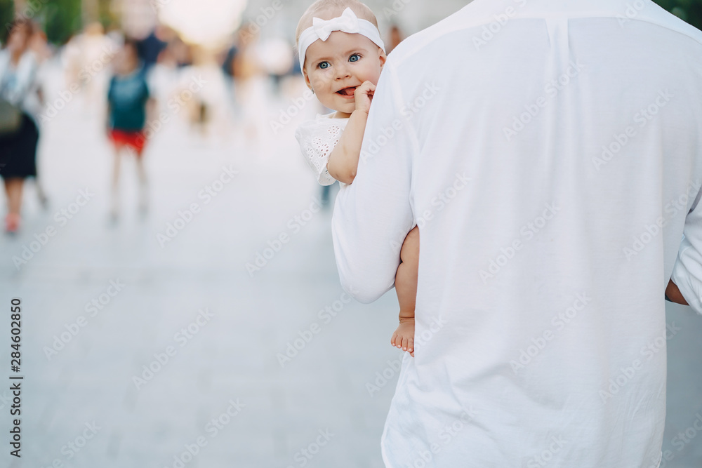 beautiful stylish young father with tattoos and a white shirt walking through the sunny city with his newborn daughter
