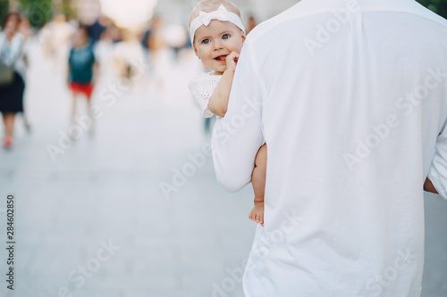 beautiful stylish young father with tattoos and a white shirt walking through the sunny city with his newborn daughter